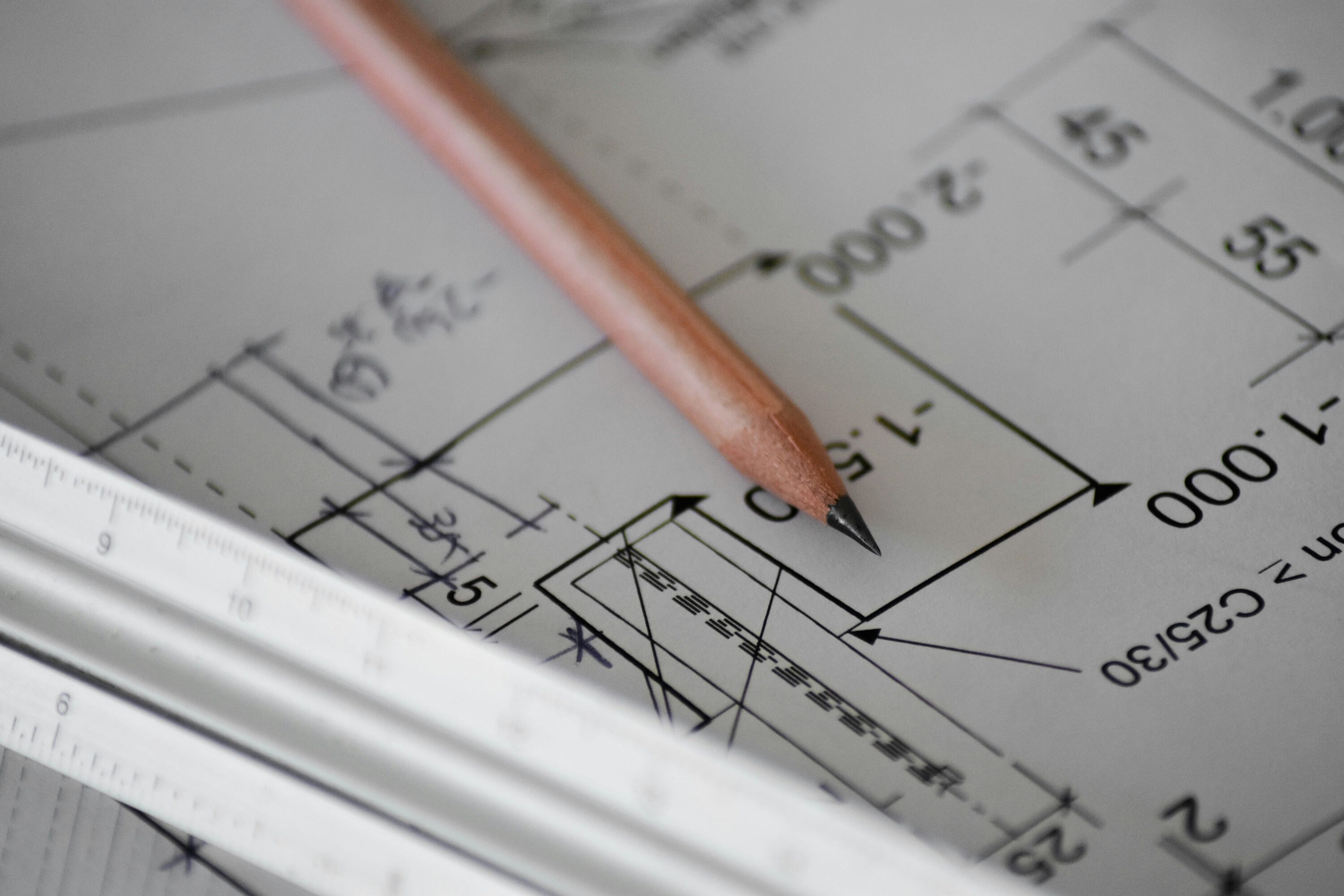 Ein Architekten-Bleistift liegt auf Plänen mit Aufmaßen – Grundlage für die Objektplanung nicht nur in der Industrie